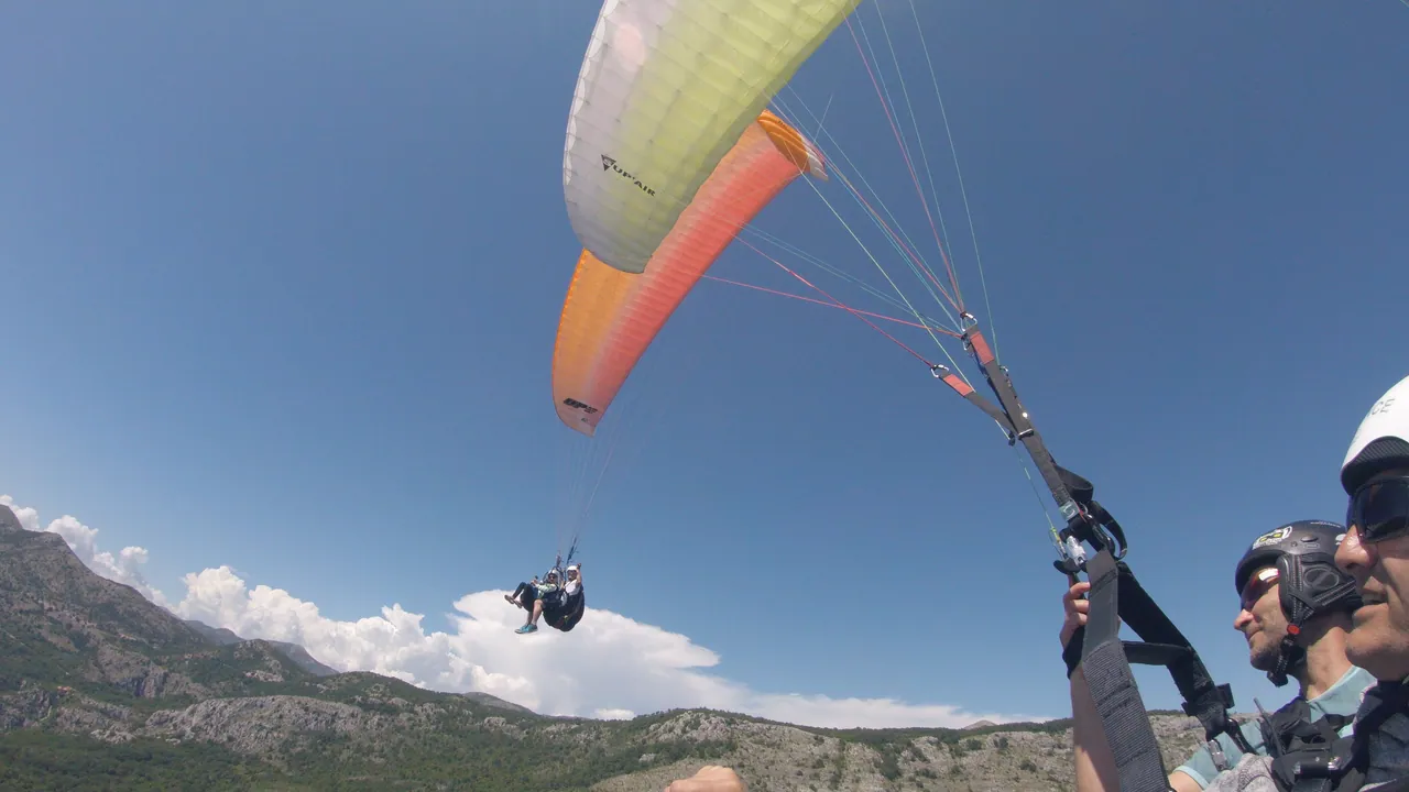 Two tandem paragliders flying above the Petrovac coastal route